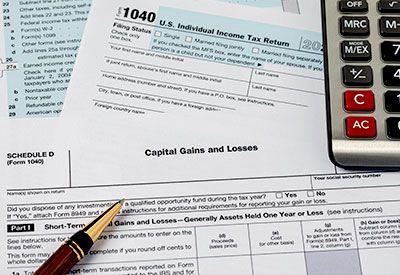 A partially completed U.S. 1040 Individual Income Tax Return form lies on a table, with a Schedule D form titled 'Capital Gains and Losses' underneath