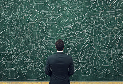 A man in a suit faces a chalkboard covered in chaotic scribbles, symbolizing the complexity and challenges of estate planning.