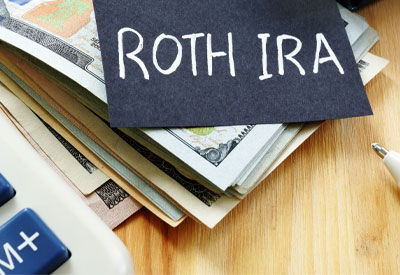 Pile of cash next to a calculator with a note reading 'Roth IRA'