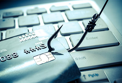 A credit card is hooked by a fishing hook, symbolizing phishing attacks, placed on a computer keyboard.