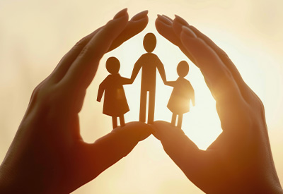 A pair of hands cupping a paper cutout family under warm sunlight, symbolizing protection and care.