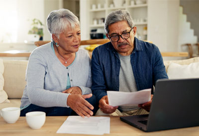 An older couple reviewing estate planning documents on a couch, discussing topics like choice of law, wills, domicile, probate, intestate succession, revocable living trusts, and multi-state property considerations