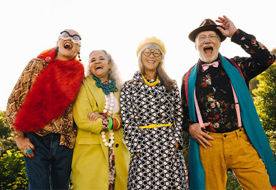 Four older adults joyfully pose outdoors, their colorful and eclectic clothing as vibrant as a strange inheritance.