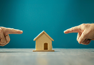 Two individuals point at a small house, symbolizing estate disputes and property ownership conflicts