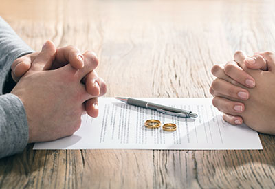 Two pairs of hands are clasped on either side of a wooden table, with a document and pen between them