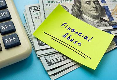A sticky note labeled 'Financial Abuse' placed over a stack of cash and a calculator, symbolizing senior financial exploitation and abuse.