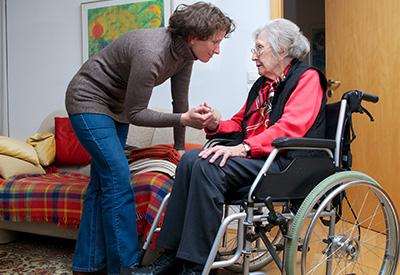 A caregiver comforts an elderly woman in a wheelchair, representing the emotional and practical challenges of guardianship and long-term care decisions without advance directives.