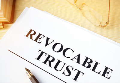 A  document titled 'Revocable Trust' rests on a wooden desk, accompanied by a pair of glasses and a pen, embodying the essentials of estate planning.