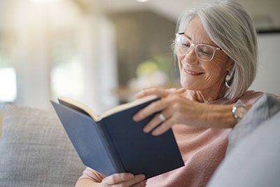 Health - Senior woman sitting on a couch reading a book