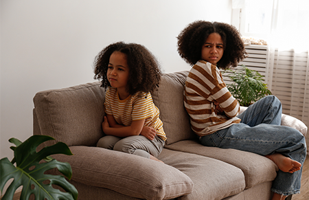 two half-siblings sitting on the couch with their backs facing each other