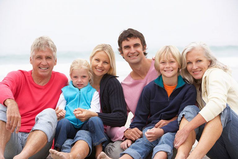 a multigenerational family sitting at the beach smiling for the camera