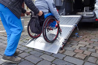 a caregiver helping a someone with a disability in a wheelchair get up a ramp