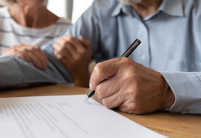 Close-up of two people seated at a table. One person is holding a pen, signing an estate planning document