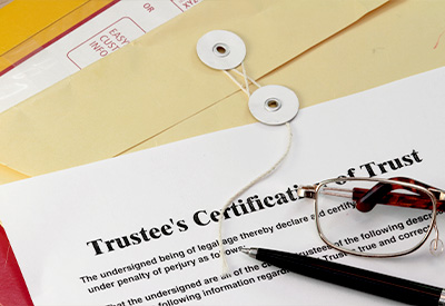 A certification of trust document sits on a desk alongside a black pen, a pair of eyeglasses, and a closed manila envelope with a string closure