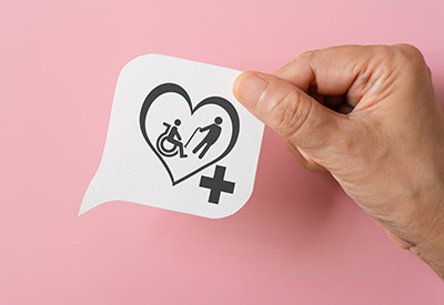 A hand holding an icon of a heart with a medical cross and caregiving figures symbolizes the role of Miller trusts in securing long-term care benefits for those in income cap states.