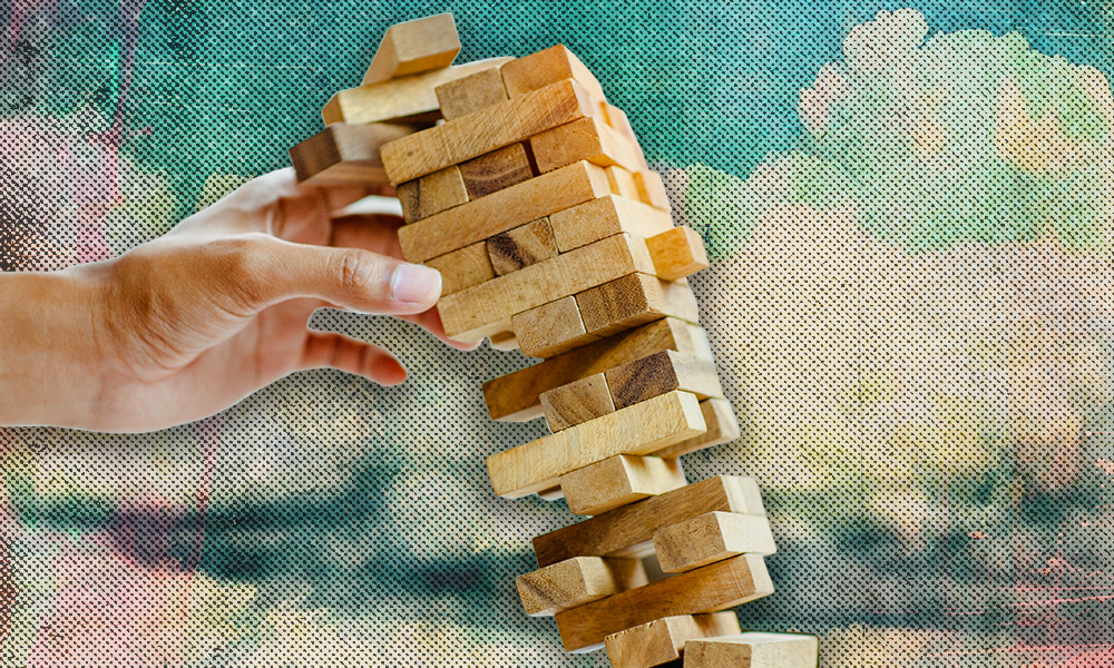 A hand pulling a block from a teetering Jenga tower, symbolizing how trust funding failures and simple mistakes can destabilize an estate plan.