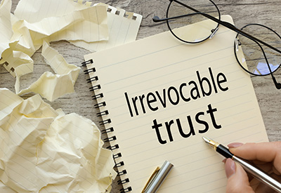 A notebook labeled 'Irrevocable trust,' with a pen and glasses, highlighting trust administration and asset protection strategies for Medicaid planning.