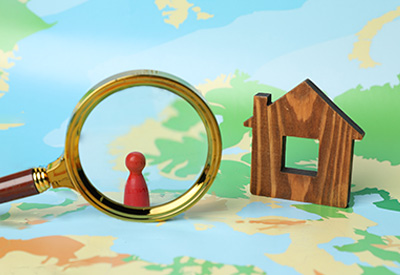 A magnifying glass focusing on a wooden house and a red game piece on a map