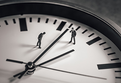 Two miniature figures standing on the hands of a large clock