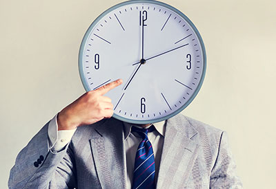 A businessman with a clock as a face, pointing to the time
