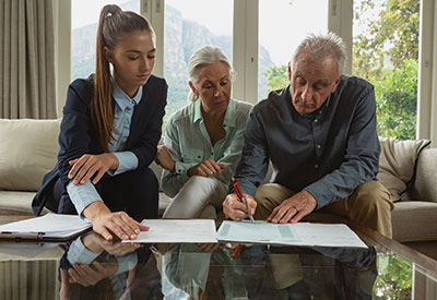 An elderly couple signing documents with a financial professional, representing estate planning, trust agreements, and asset protection.