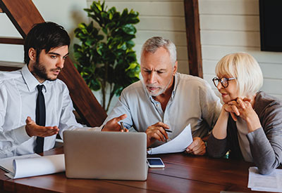 A senior couple reviewing financial documents with an advisor on a laptop, symbolizing trust administration, beneficiary rights, and tax benefits.