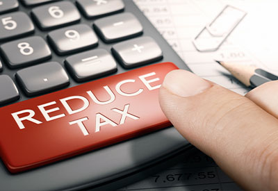 A close-up of a finger pressing a large red button labeled 'REDUCE TAX' on a calculator