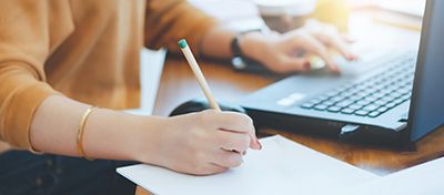 someone working on the computer while writing notes on paper