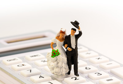 A bride and groom figurine standing on a calculator, representing joint ownership and financial planning in marriage.