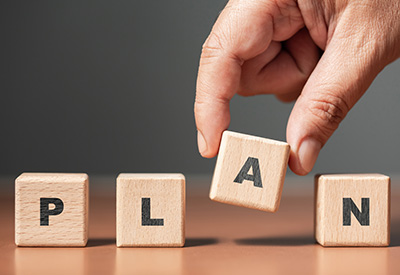 A close-up of a hand arranging wooden blocks that spell 'PLAN,' symbolizing the careful and deliberate process of estate planning.