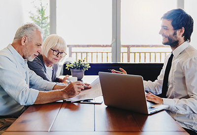 An older couple sitting at a table with a professional advisor, reviewing documents on a laptop