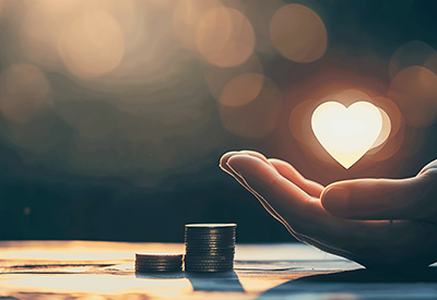 A hand holding a glowing heart beside stacked coins, representing fairness and care in financial planning and inheritance distribution.