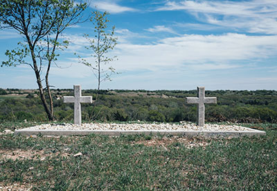 A grassy landscape with two stone crosses marks a poignant reminder of survivorship on a small, pebbled area.