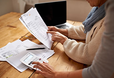 Two people sit at a wooden table reviewing financial documents, meticulously planning for state estate taxes. One holds papers while the other points at them