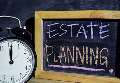 A blackboard with 'ESTATE PLANNING' in chalk stands beside a vintage alarm clock