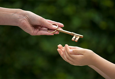 An adult hand is passing an old-fashioned, gold key to a child's outstretched hands against a blurred green background