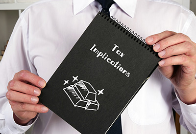 person holding a black notebook labeled 'Tax Implications' with a financial icon, suggesting guidance on asset transfer and gifting consequences.