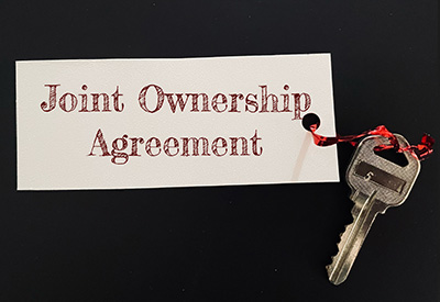 A key attached to a tag labeled 'Joint Ownership Agreement,' highlighting the risks and considerations of joint ownership in estate planning.