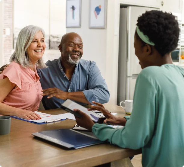 Smiling senior couple sitting at a table with a consultant, discussing documents and services.